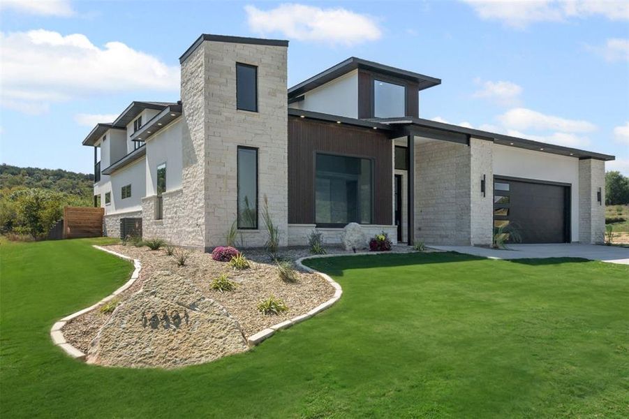 Modern home featuring stone siding, a garage, a front yard, concrete driveway, and stucco siding