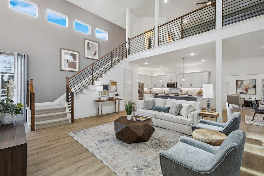 Open-concept living area featuring a two-story ceiling, wood-finish flooring, a contemporary staircase with wood and metal railing, a second-story loft, and recessed lighting