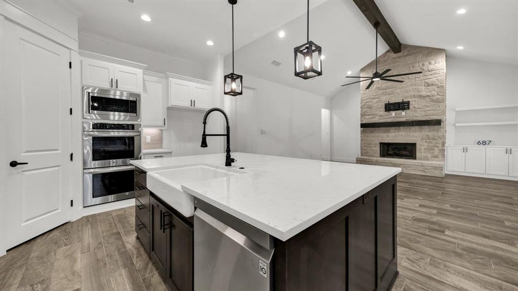 Kitchen featuring appliances with stainless steel finishes, beam ceiling, light wood-type flooring, a fireplace, and ceiling fan