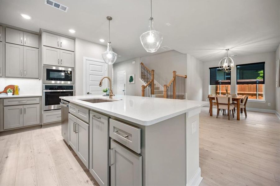 Kitchen with gray cabinets, light wood-type flooring, stainless steel appliances, light countertops, and a chandelier Kitchen with gray cabinets, light wood-type flooring, stainless steel appliances, light countertops, and a chandelier