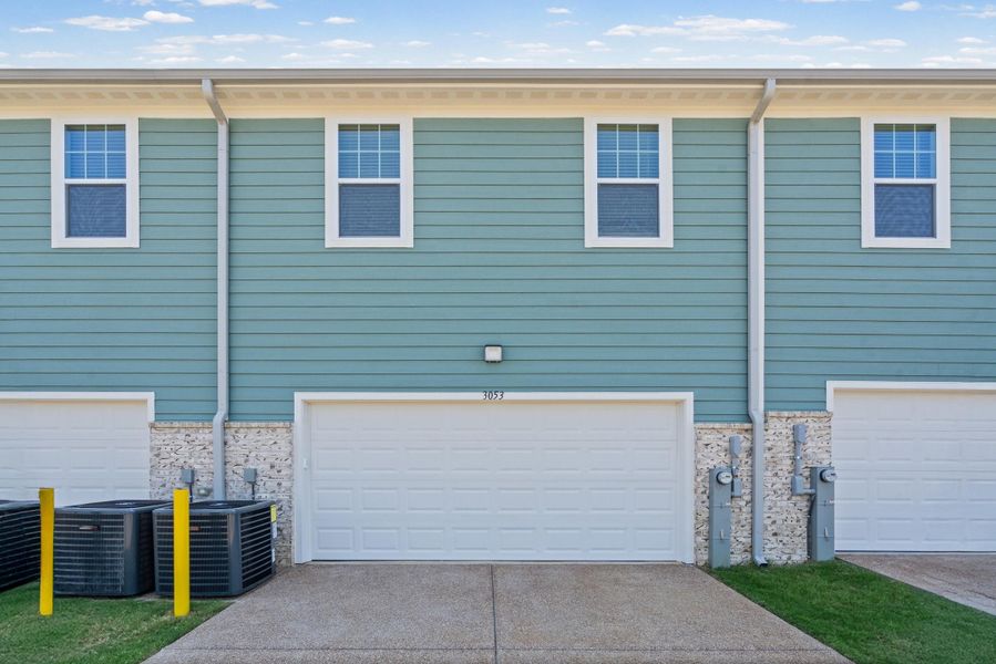 Exterior featuring teal siding, multiple windows, a white garage door, concrete driveway, and stone accents