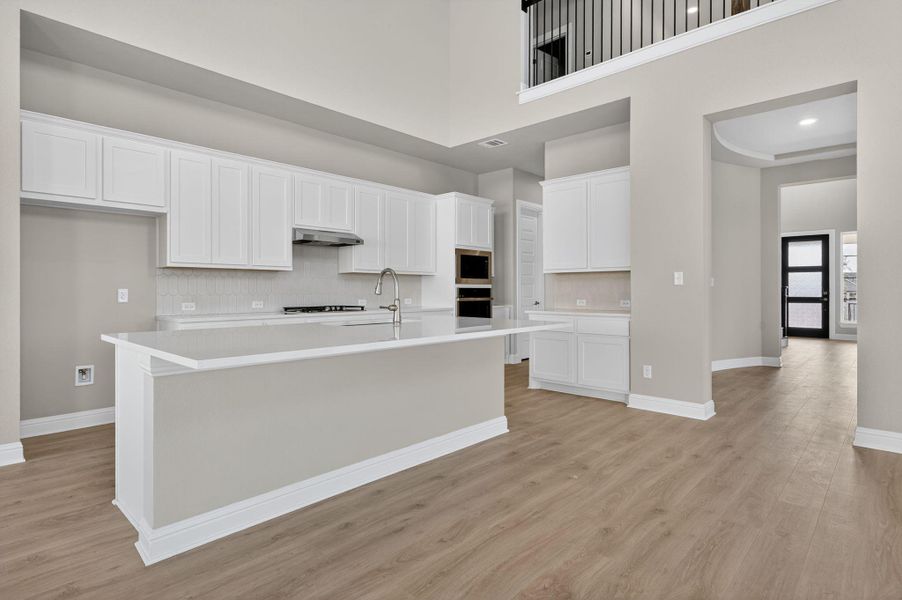 Kitchen with white cabinetry, backsplash, light wood-style flooring, a kitchen island with sink, and a towering ceiling