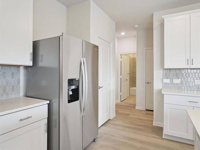 Kitchen featuring decorative backsplash, white cabinetry, stainless steel fridge, and light wood-style floors