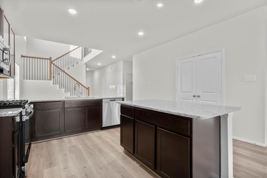 Another perspective of the kitchen showcases the generous counter space and central island that connects seamlessly to the family room and staircase beyond. This elegant design encourages both functionality and togetherness in the heart of the home. Another perspective of the kitchen showcases the generous counter space and central island that connects seamlessly to the family room and staircase beyond. This elegant design encourages both functionality and togetherness in the heart of the home.