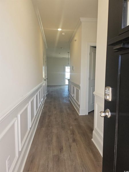 Hallway featuring a decorative wall, a wainscoted wall, ornamental molding, and dark wood-style flooring