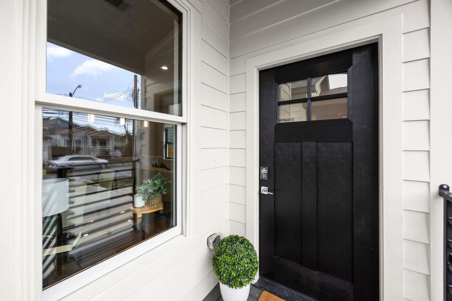 This inviting front entry features a bold black door with glass accents, a modern keypad lock, and a charming covered porch, offering both security and style.