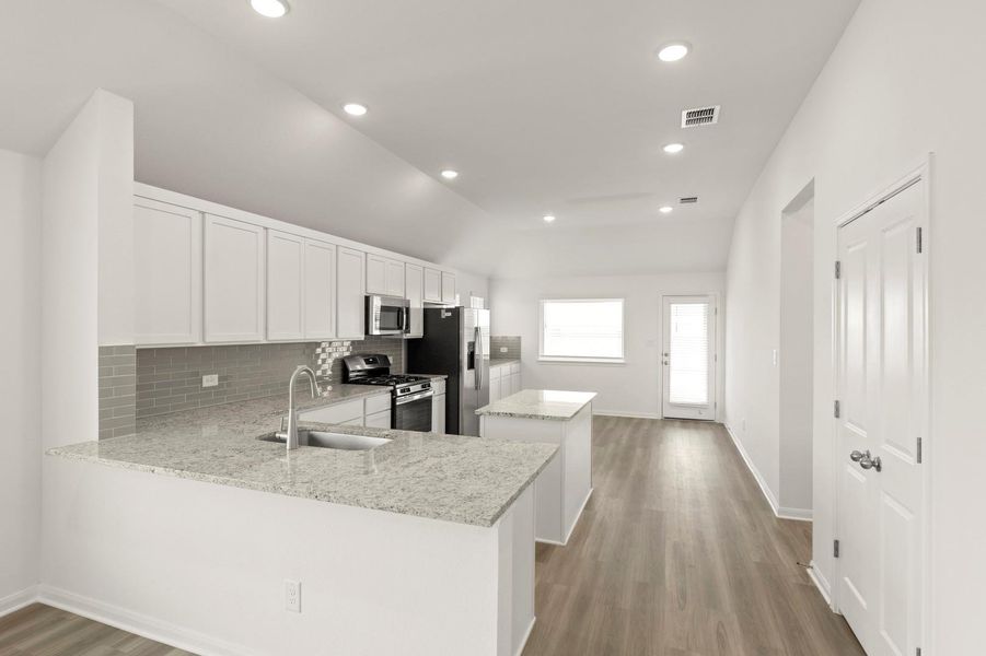 Kitchen with a center island, white cabinets, backsplash, appliances with stainless steel finishes, and lofted ceiling