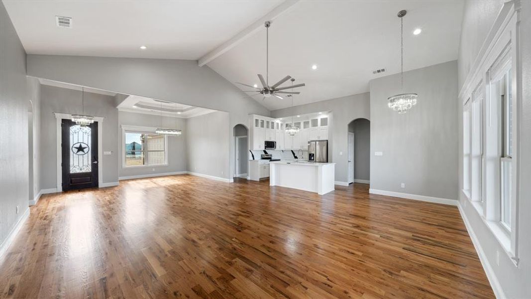 Unfurnished living room featuring visible vents, arched walkways, wood finished floors, and ceiling fan with notable chandelier