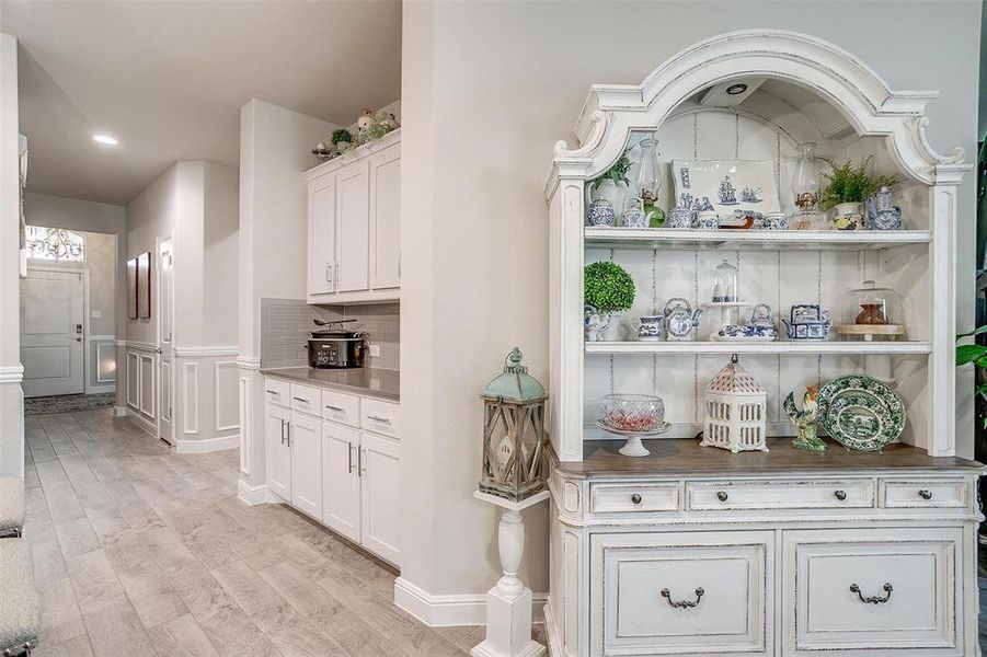 Bar with light wood finished floors, wainscoting, decorative backsplash, and a decorative wall