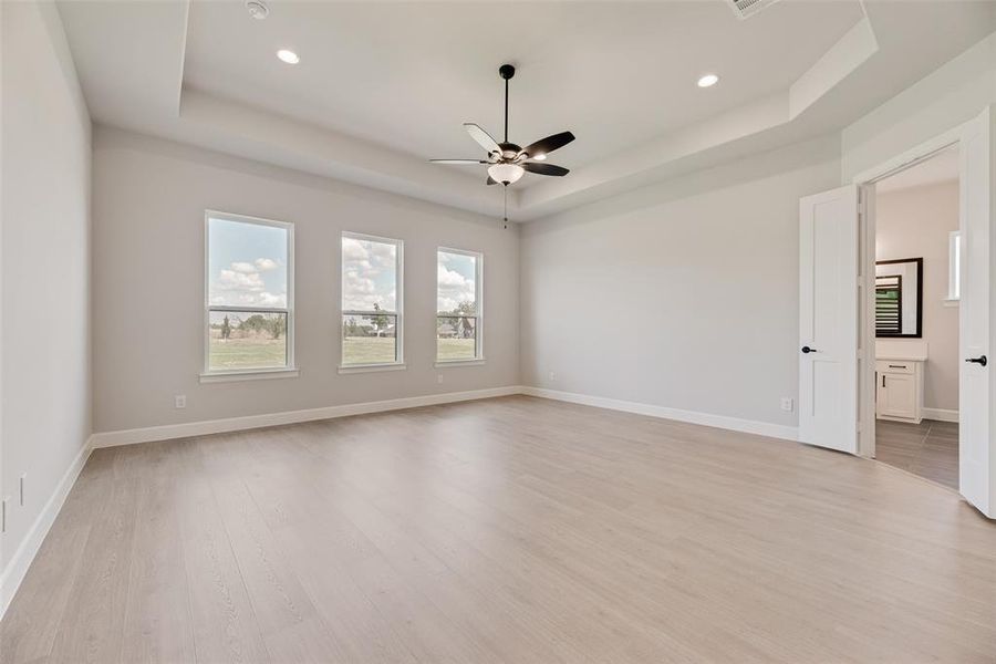 Unfurnished room featuring a raised ceiling, light wood-style floors, a ceiling fan, and recessed lighting