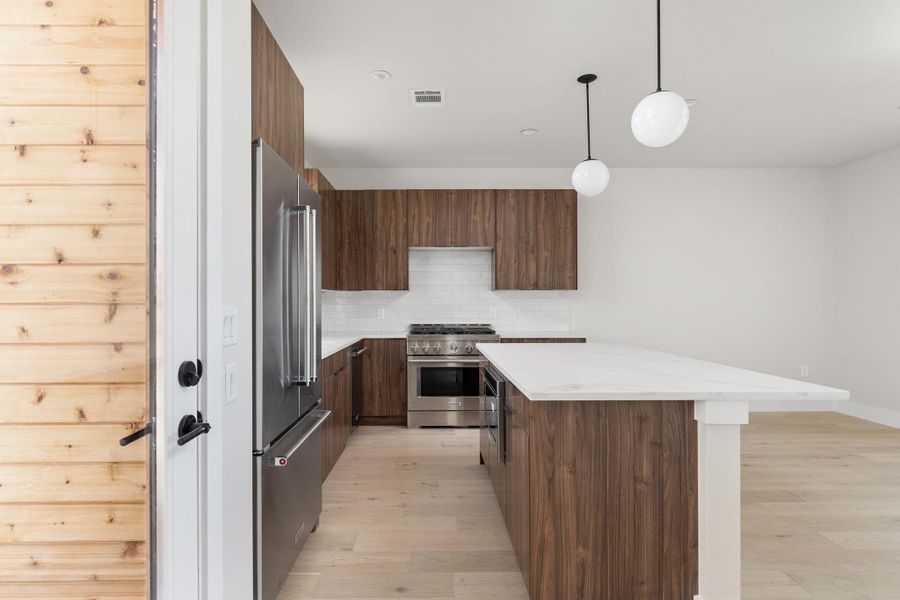 Kitchen featuring tasteful backsplash, a kitchen island, light wood-type flooring, premium appliances, and modern cabinets