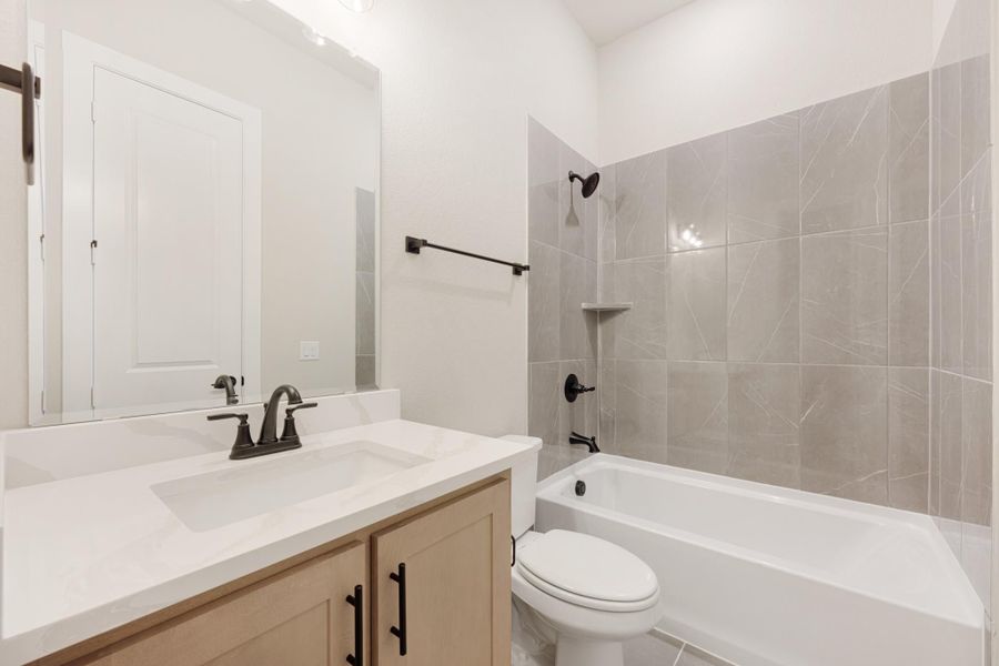 Bathroom with single vanity, white countertop, tub-shower combo with gray tile surround, and toilet