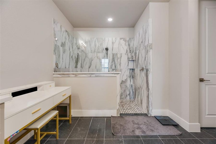 Spacious walk-in shower featuring large format marble-look tile, a built-in niche, and a contrasting mosaic tile floor