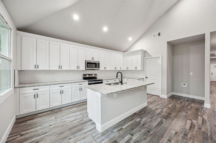 Kitchen featuring high vaulted ceiling, white cabinetry, granite countertops, tasteful backsplash, stainless steel appliances, and light stone counters