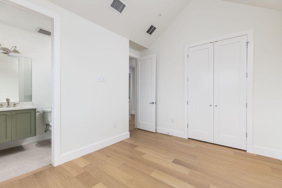 Unfurnished bedroom featuring light wood-type flooring, ensuite bath, and a high ceiling