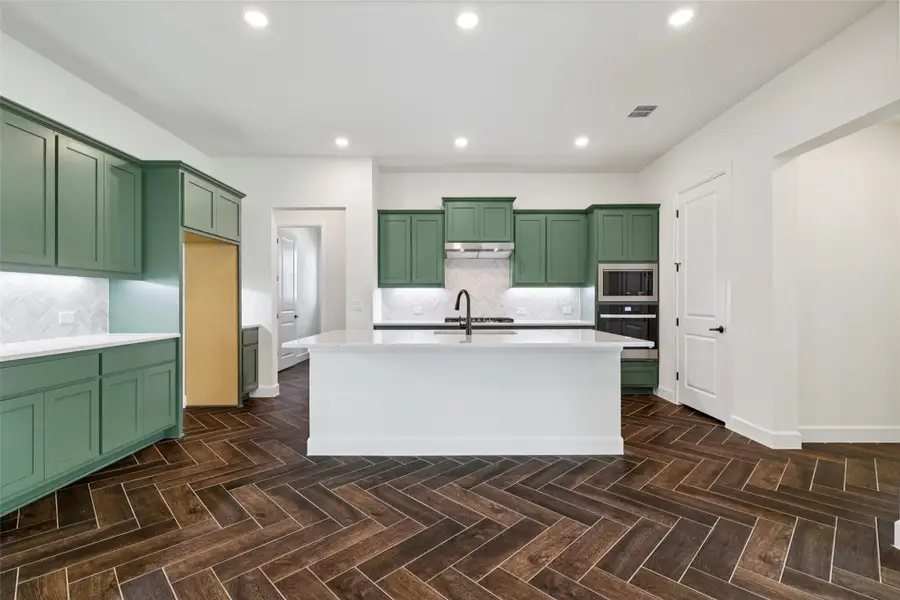 Kitchen with green cabinets, light countertops, decorative backsplash, black oven, and recessed lighting Kitchen with green cabinets, light countertops, decorative backsplash, black oven, and recessed lighting