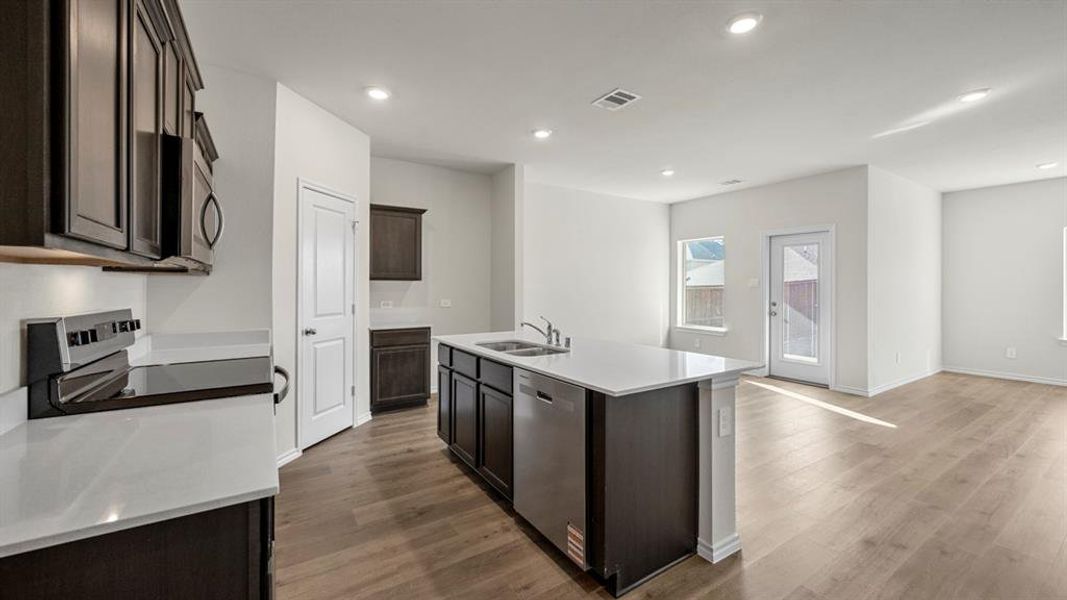Kitchen with dark wood finish cabinetry, an island with sink, stainless steel appliances, recessed lighting, and dark wood-type flooring