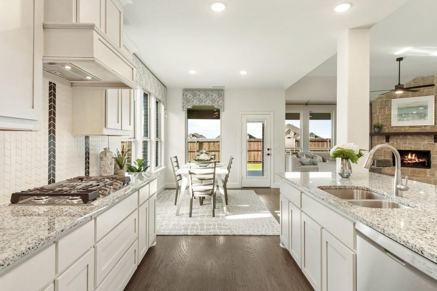 Open kitchen with white cabinets, granite countertops, gas cooktop, and view into dining area and living room with stone fireplace.