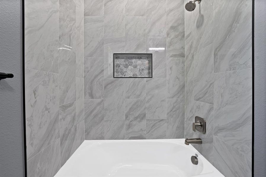 Bathtub and shower combination featuring large format tile surrounds, a built-in shower niche with mosaic tile inlay, and brushed nickel fixtures