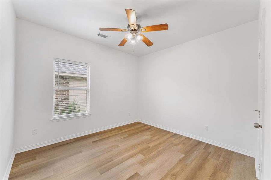 Room featuring wood-finish flooring, white baseboards, a white ceiling fan with integrated lighting, and a window with blinds