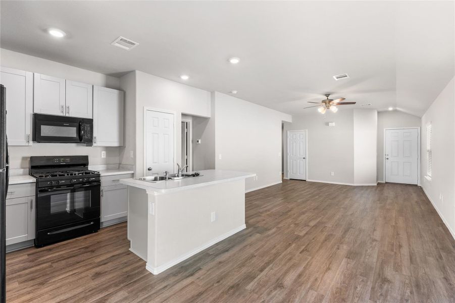 Open-concept kitchen with center island, gas range, and adjacent living area. Open-concept kitchen with center island, gas range, and adjacent living area.
