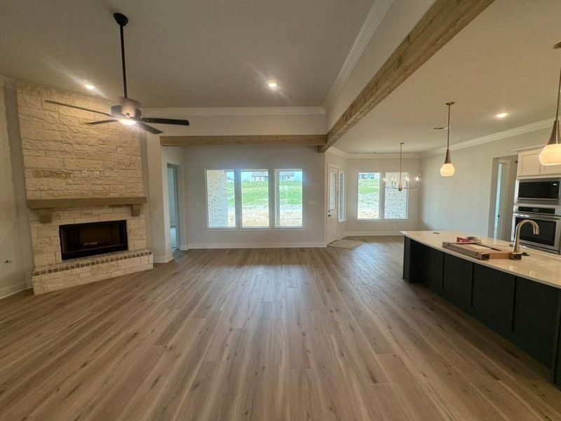 Open-concept living space featuring wood-finish flooring, a stone-clad fireplace with a wood mantle, and a ceiling fan Open-concept living space featuring wood-finish flooring, a stone-clad fireplace with a wood mantle, and a ceiling fan