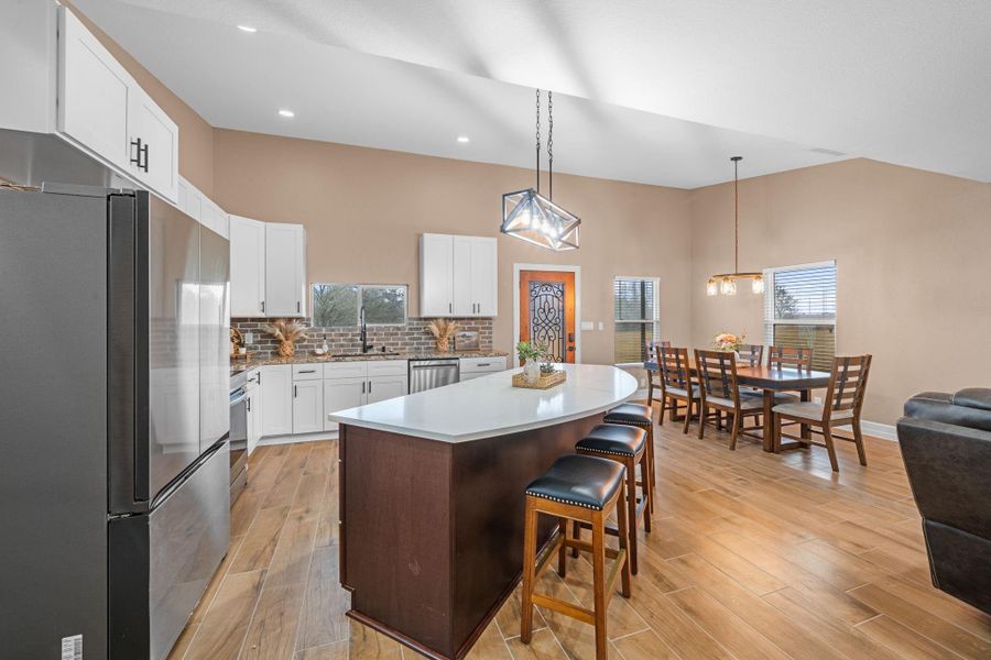 This kitchen features a massive, curved center island with a crisp white countertop and deep chocolate cabinetry, providing both a sprawling prep surface and a natural gathering spot for guests.