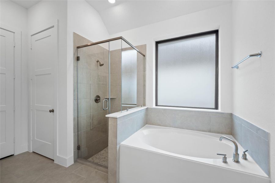 This alternate view of the primary bathroom showcases a walk-in shower with a stylish tile surround, a separate garden tub perfect for unwinding after a long day, and a large rain glass window that provides natural light while maintaining privacy.