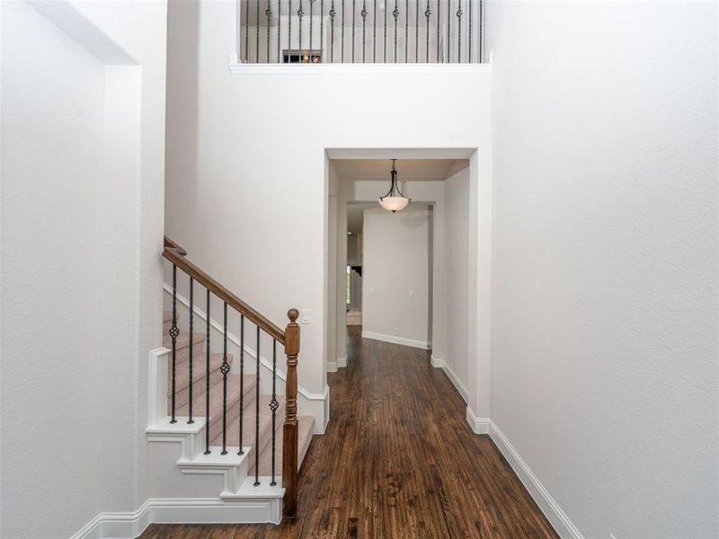 Hallway featuring dark wood-style floors, a towering ceiling, and stairs Hallway featuring dark wood-style floors, a towering ceiling, and stairs