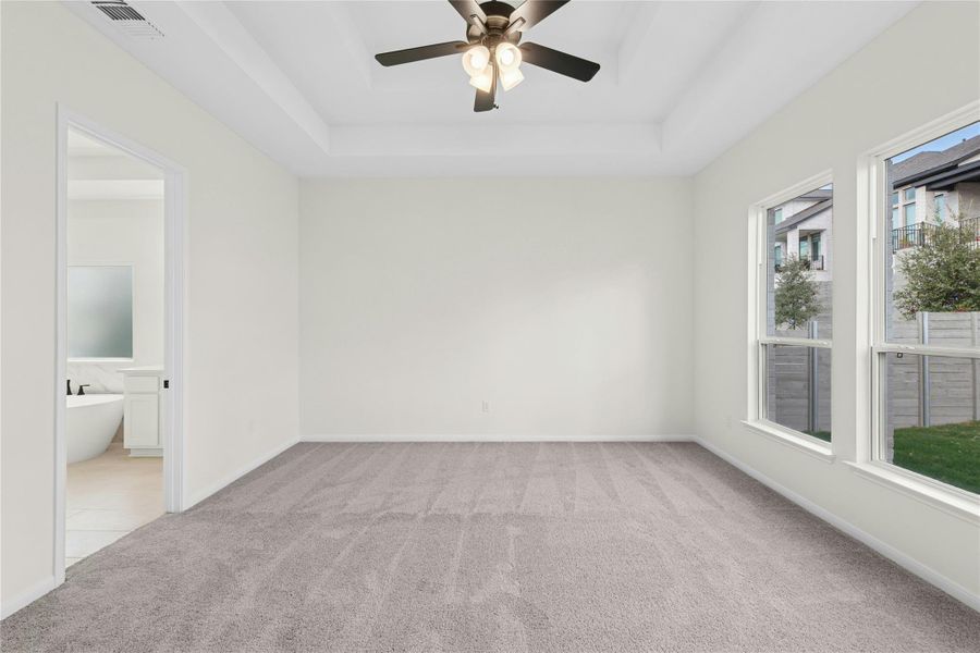 Unfurnished bedroom with a tray ceiling, light colored carpet, a ceiling fan, and ensuite bathroom Unfurnished bedroom with a tray ceiling, light colored carpet, a ceiling fan, and ensuite bathroom