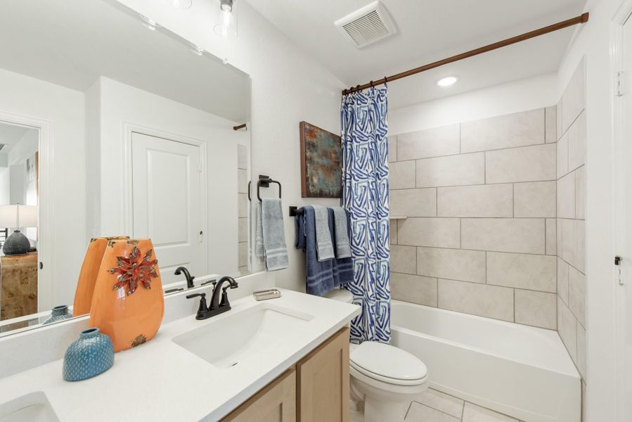 Bathroom with single vanity, white countertop, tiled tub-shower combo with curtain, and toilet Bathroom with single vanity, white countertop, tiled tub-shower combo with curtain, and toilet
