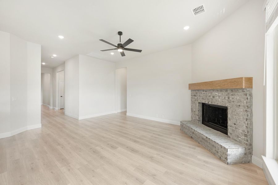 Empty living room with light wood floors, ceiling fan, and stone fireplace with wood mantel