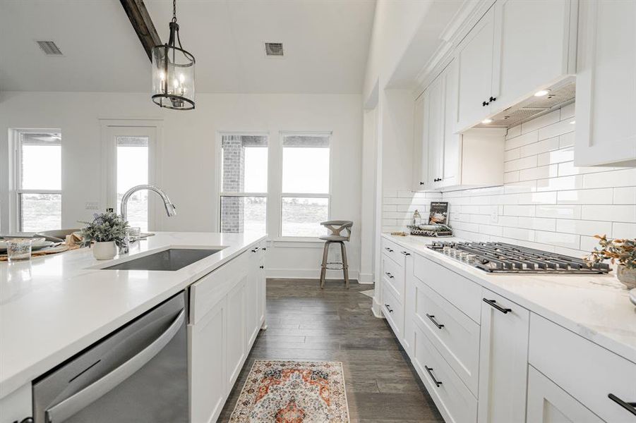 Kitchen featuring dark wood-type flooring, sink, white cabinetry, hanging light fixtures, and appliances with stainless steel finishes