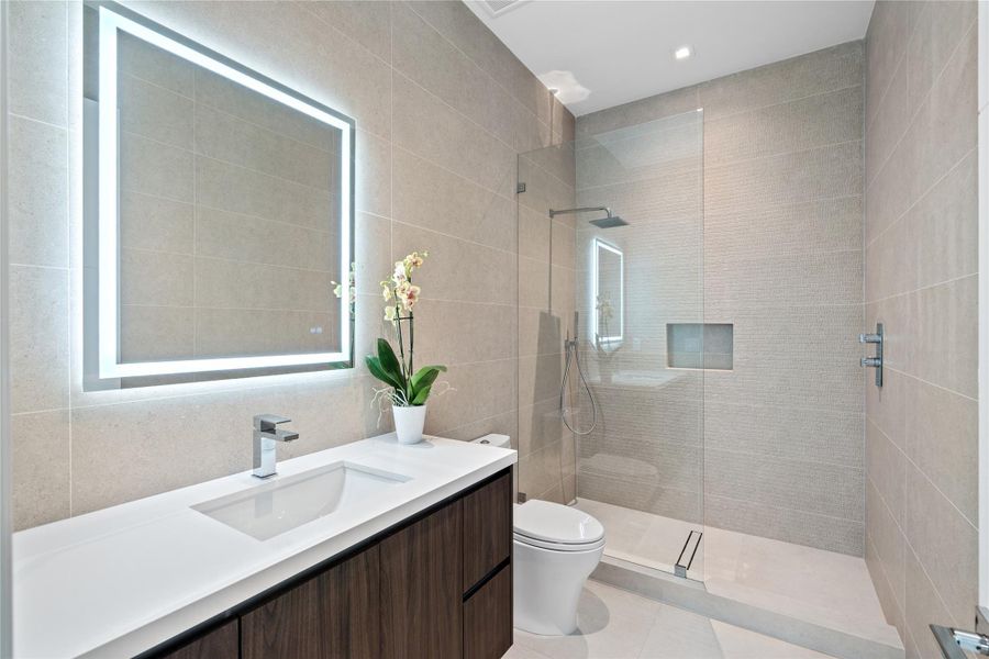 Sleek modern bathroom with glass-enclosed shower, vanity, and illuminated LED mirror. Sleek modern bathroom with glass-enclosed shower, vanity, and illuminated LED mirror.