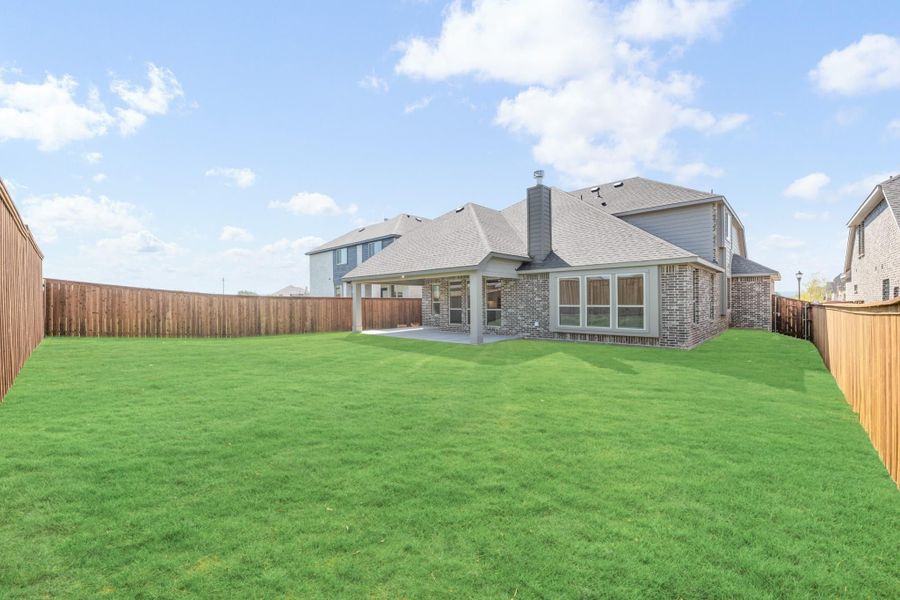 Backyard of brick home with large grass lawn, covered patio, and wood privacy fence
