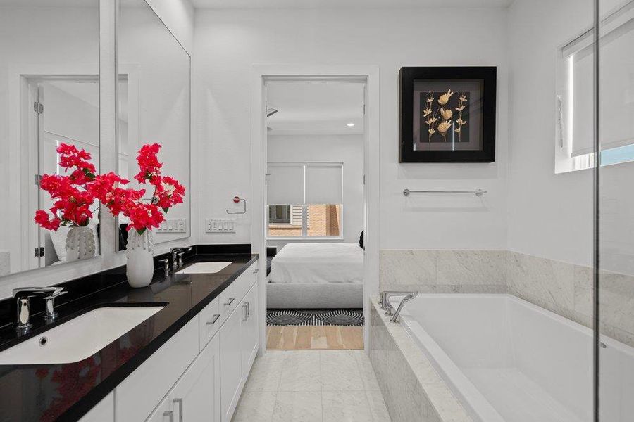 Dual vanity with sleek black counters complement the inviting, deep soaking tub in this serene bath. Dual vanity with sleek black counters complement the inviting, deep soaking tub in this serene bath.
