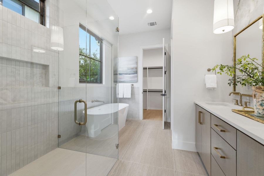 Bathroom featuring double vanity, a walk-in stall, a soaking tub, a spacious closet, and tile walls