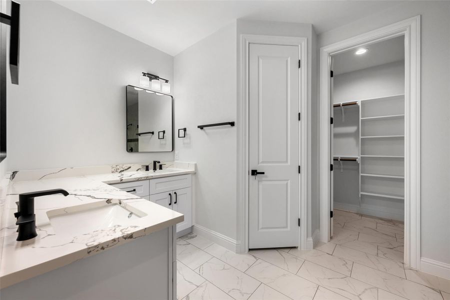 Bathroom with light marble finish floors, double vanity, and a spacious closet