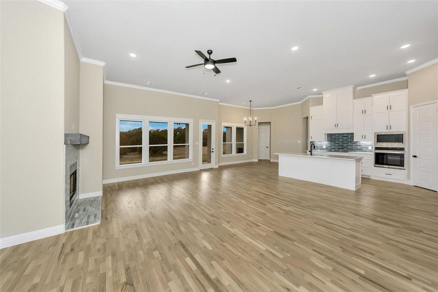 Unfurnished living room featuring ceiling fan with notable chandelier, light hardwood / wood-style flooring, crown molding, and sink