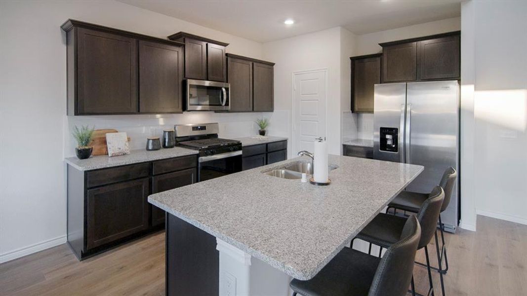 Spacious kitchen featuring an island with a dual-basin sink, dark wood cabinetry, stainless steel appliances, and wood-finish flooring Spacious kitchen featuring an island with a dual-basin sink, dark wood cabinetry, stainless steel appliances, and wood-finish flooring