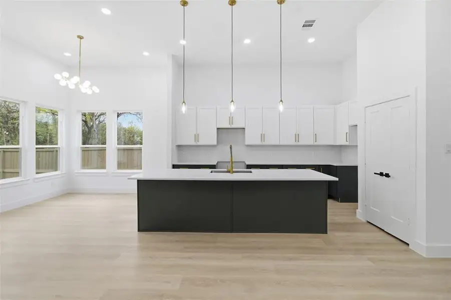 Kitchen with white cabinetry, a towering ceiling, dark cabinets, hanging light fixtures, and light wood-style floors