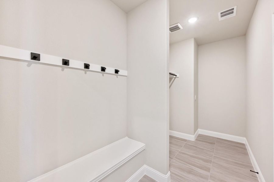 Mudroom with built-in bench, black wall hooks, and tile floors leading to a closet area Mudroom with built-in bench, black wall hooks, and tile floors leading to a closet area