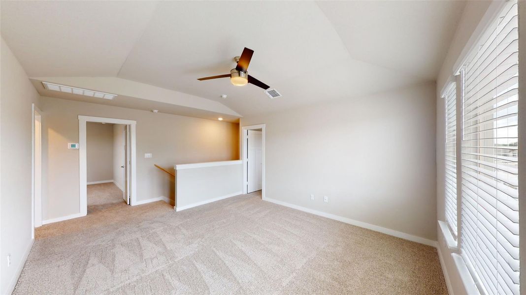 Empty room with vaulted ceiling, light carpet, and ceiling fan