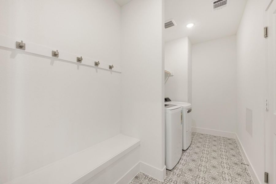 Mudroom with wall hooks and bench leading to laundry area with washer and dryer on patterned tile floor