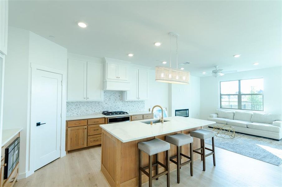 Kitchen with brown cabinetry, a kitchen bar, open floor plan, a center island with sink, and hanging light fixtures