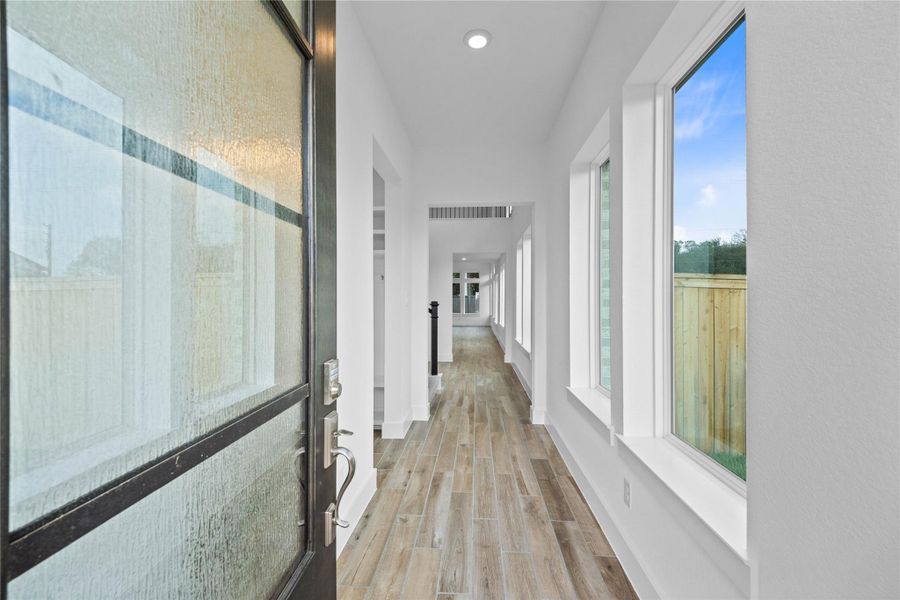 A bright and open interior entryway focuses on modern design and natural light. The space is amplified by high ceilings, recessed lighting, and generous natural light pouring in from large windows, creating an airy and welcoming first impression.