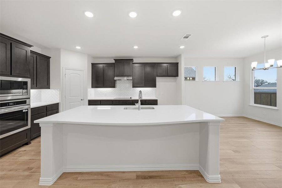 Kitchen featuring backsplash, stainless steel appliances, light wood-type flooring, and light stone countertops