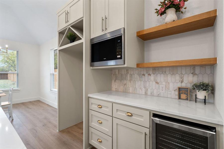 Kitchen with open shelves, stainless steel microwave, light stone countertops, beverage cooler, and tasteful backsplash Kitchen with open shelves, stainless steel microwave, light stone countertops, beverage cooler, and tasteful backsplash