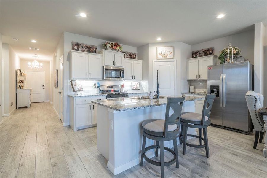 Kitchen with light stone countertops, an island with sink, appliances with stainless steel finishes, tasteful backsplash, and white cabinetry