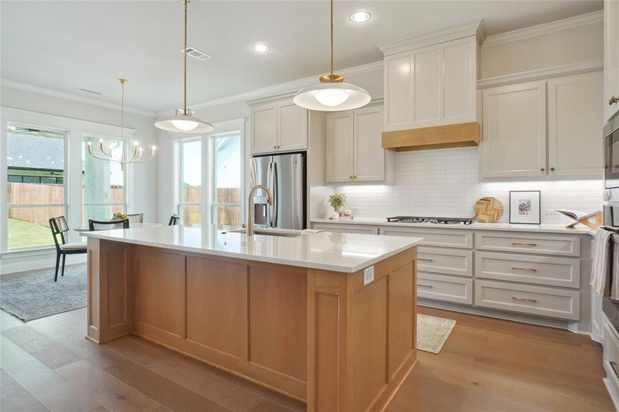 Kitchen with white cabinetry, light hardwood / wood-style flooring, tasteful backsplash, an island with sink, and stainless steel appliances